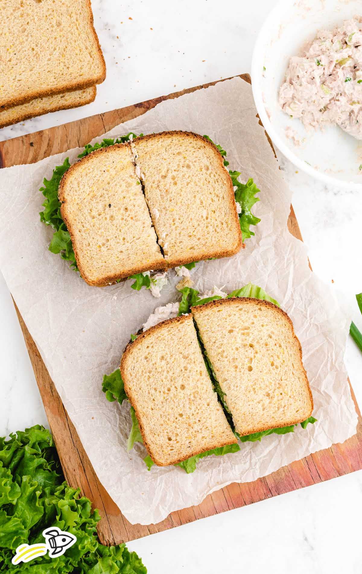 overhead shot of tuna sandwich sliced on a sheet that is placed on a wooden board