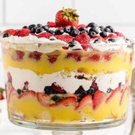 close up shot of vanilla trifle in a clear dish with strawberries and blackberries on top