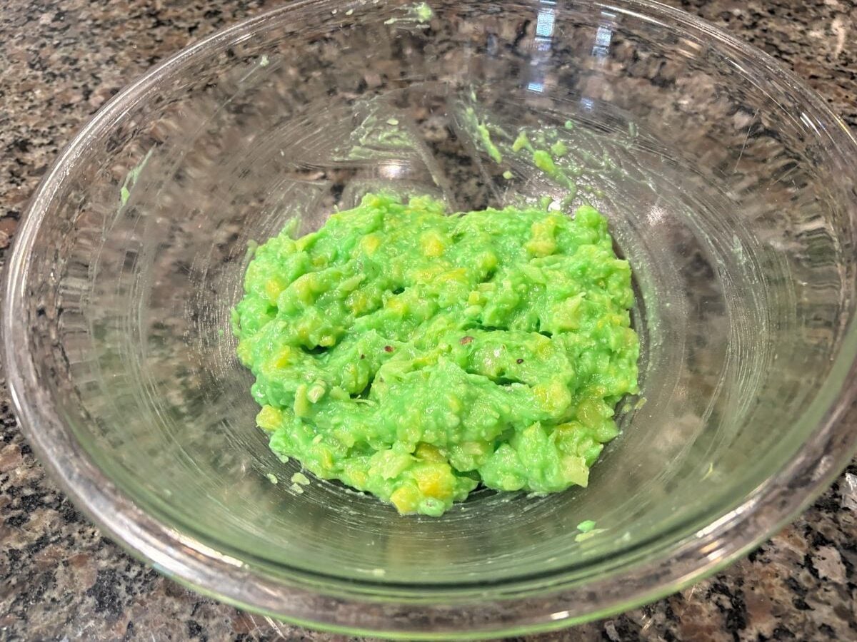 A clear glass bowl on a granite countertop contains a small amount of chunky, bright green guacamole&mdash;though unlike the sweet Watergate Salad, this savory dip is perfect for your next gathering.