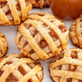 Plate of apple pie cookies with flaky crust and sugary tops, served beside a dish of caramel sauce.