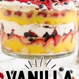 A layered Vanilla Trifle with berries, whipped cream, and custard in a glass bowl. Text reads No baking required! Vanilla Trifle Recipe. Spoons and plates are on the table next to the dessert.