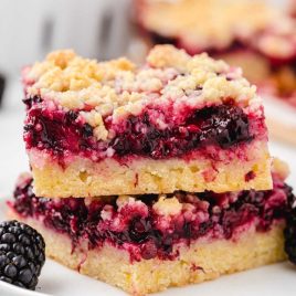 close up shot of Blackberry Pie Bars stacked on top of each other on a plate with blackberries