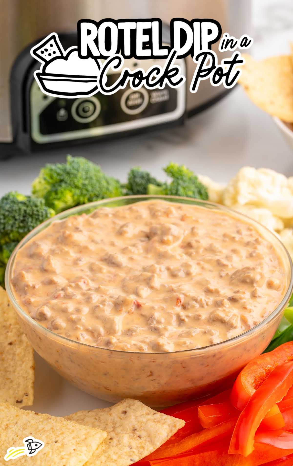 Crockpot Rotel dip in a bowl with veggies and chips, next to a slow cooker.