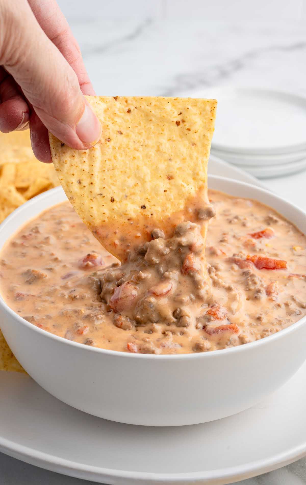 Hand dipping chip into thick and cheesy beef Rotel dip.