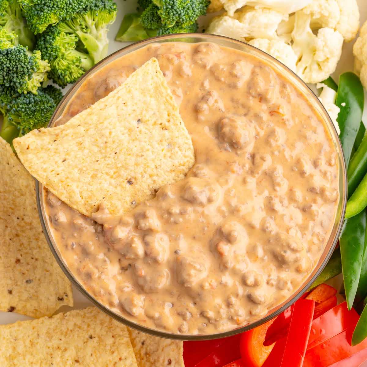 Glass bowl of beef Rotel dip with tortilla chips and vegetables on the side.