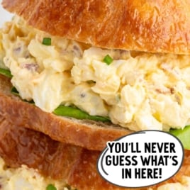 Stacked croissant sandwiches filled with egg salad and lettuce with text overlay “The Best Ever Secret Ingredient Egg Salad Recipe.”