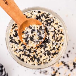 close up overhead shot of everything bagel seasoning in a clear jar with a small wooden spoon