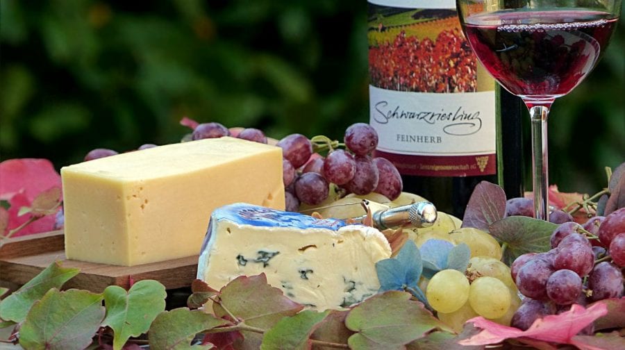 cheese platter with different types of cheese, red and green grapes, bottle of red wine and a glass of red wine