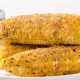 Close-up of golden, crispy fried corn on the cob stacked on a white plate