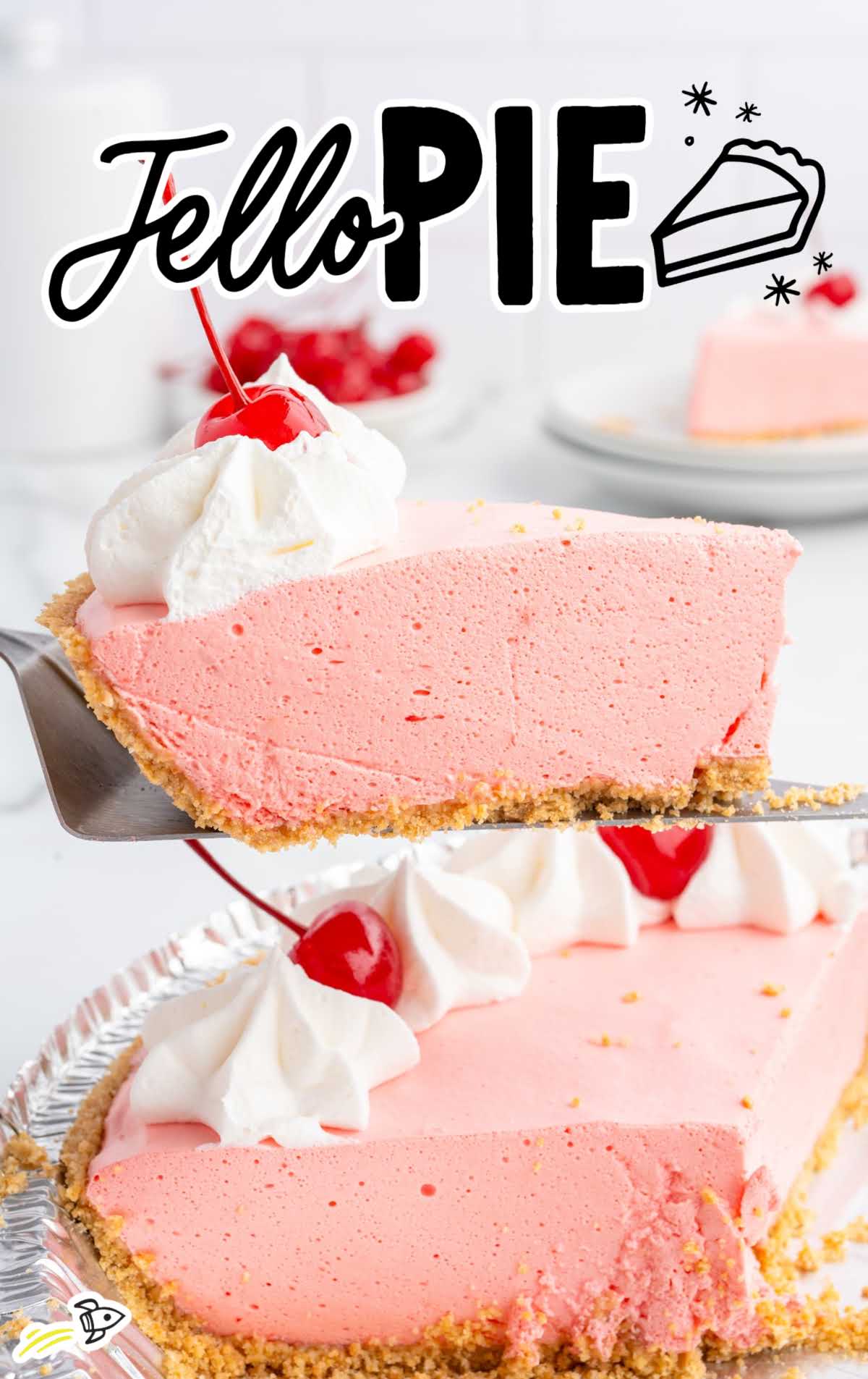 Close-up of a pink jello pie slice on a pie server, topped with whipped cream and a cherry, with the pie in the background.