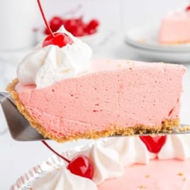 Jello pie slice with whipped topping and cherry being lifted from a pie tin, served on a pie server.