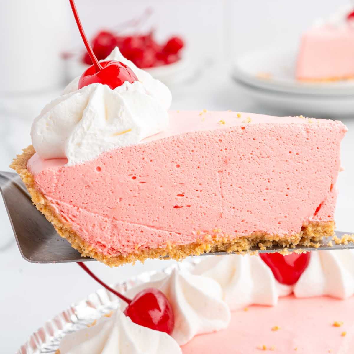Jello pie slice with whipped topping and cherry being lifted from a pie tin, served on a pie server.