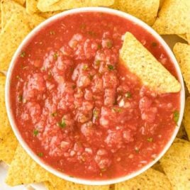 close up overhead shot of a bowl of salsa with a tortilla chip being dipped into it and surrounding it