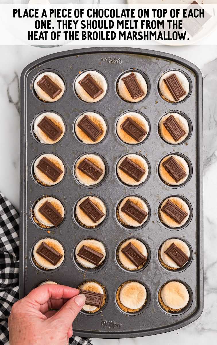 s'mores bites process shot of pieces of Hershey's being placed on top off browned marshmallows in cupcake pan