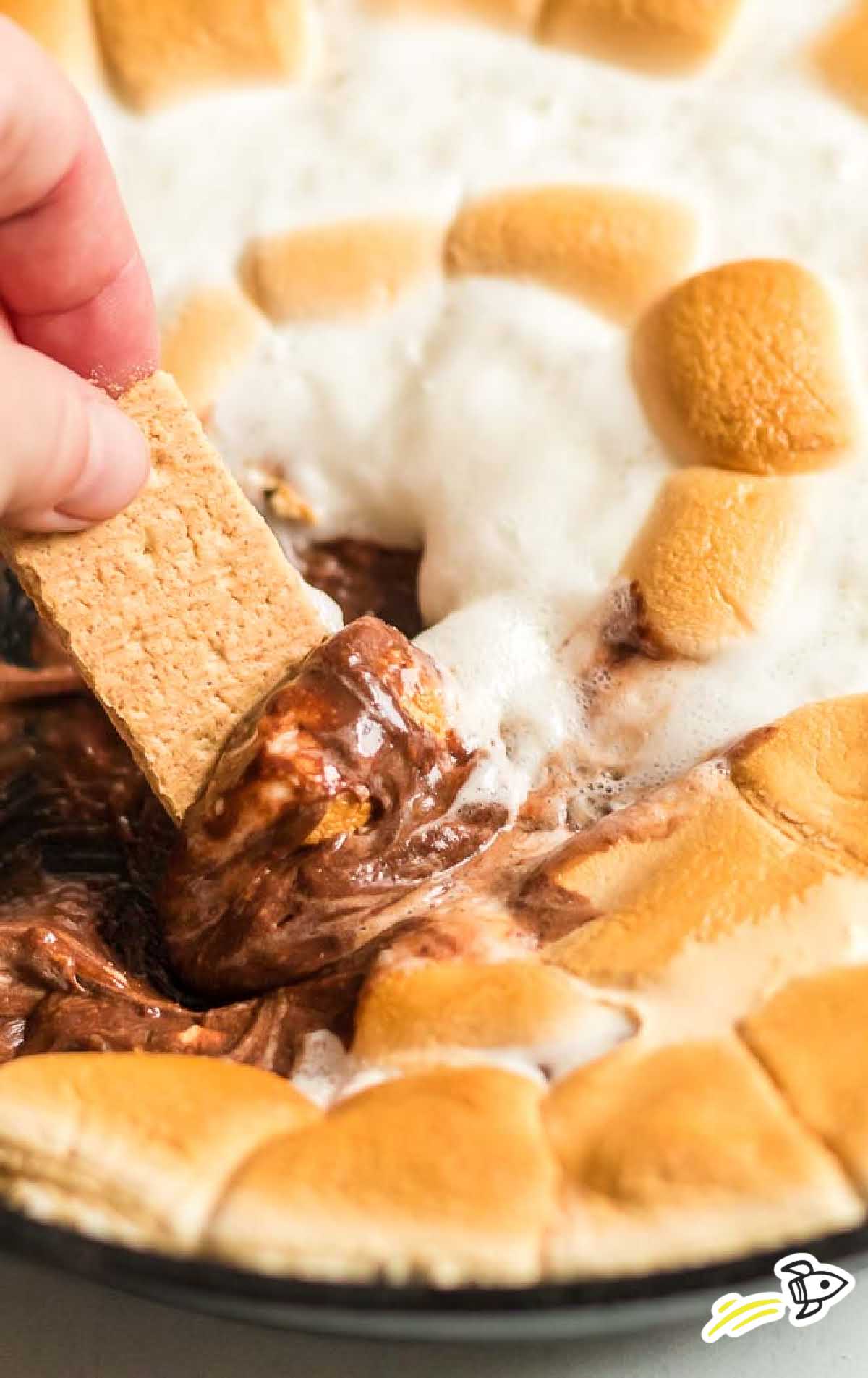 close up shot of a pan of s'mores dip with a graham cracker being dipped into the dip