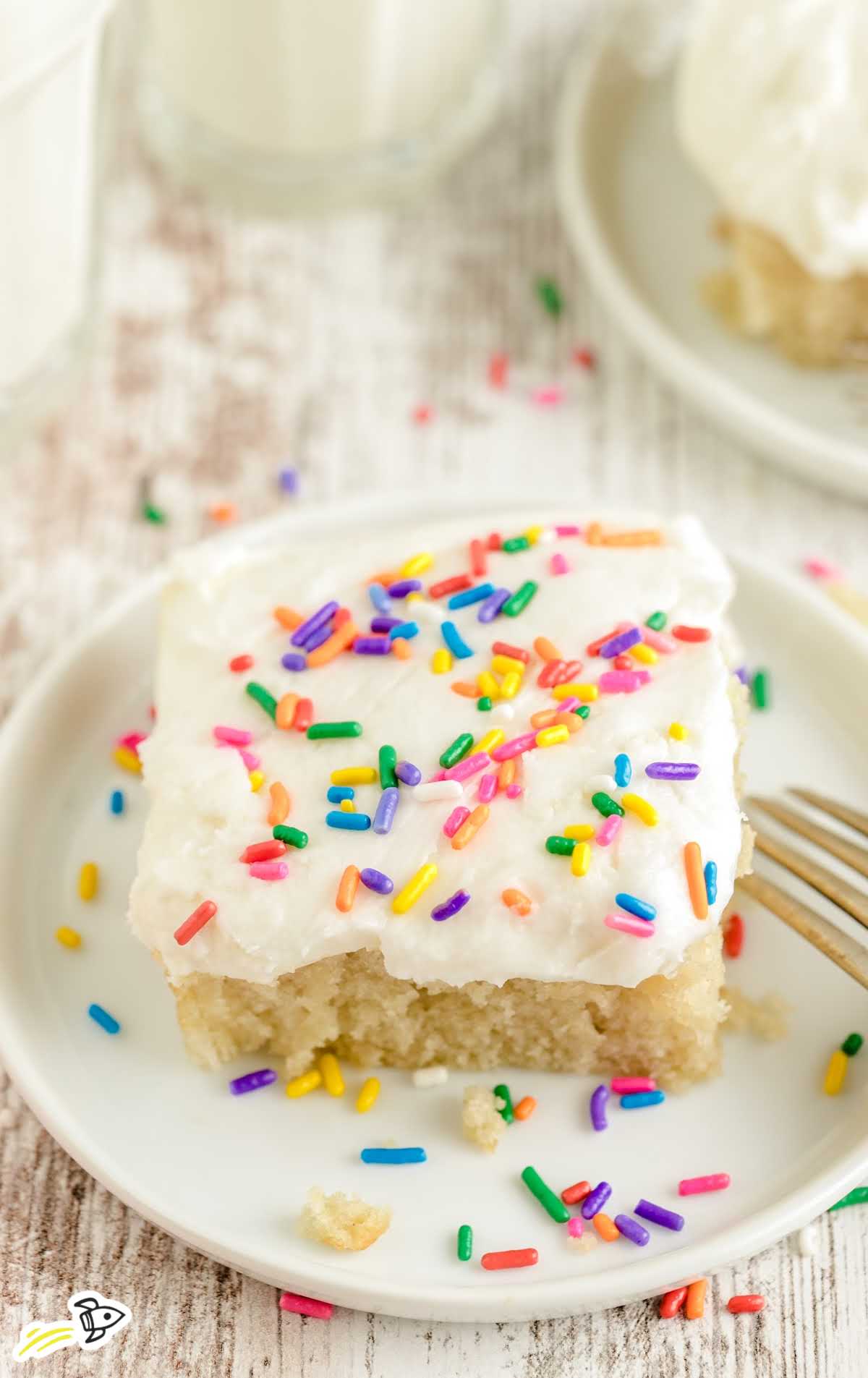 Overhead image of a slice of vanilla crazy cake with rainbow sprinkles and a bite taken out, styled on a rustic wood background.
