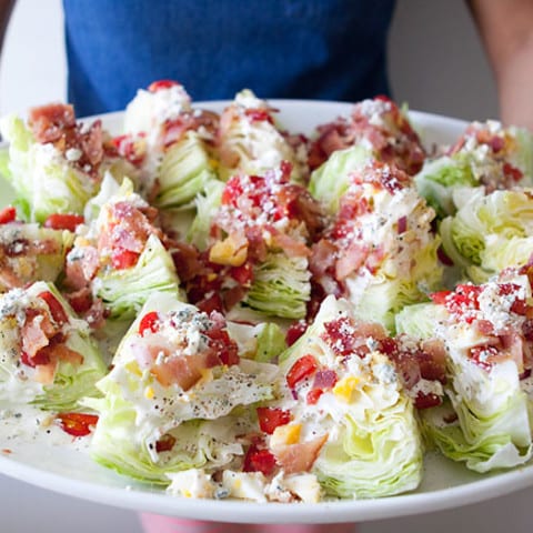 wedges of iceberg lettuce topped with meats and cheese and sauce on a platter