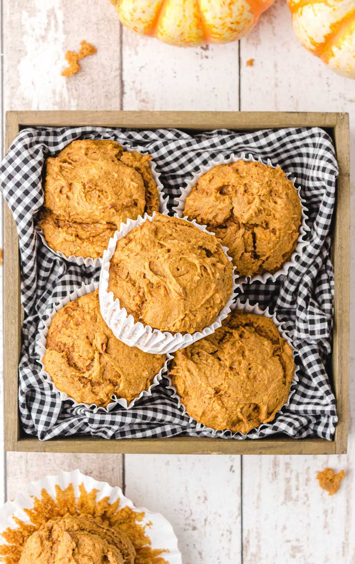 Overhead view of pumpkin spice muffins in white paper liners arranged in a wooden box with black and white gingham cloth.