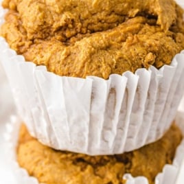 Stacked pumpkin spice muffins in white liners with text overlay โIn the oven in 2 minutes, 2 ingredient pumpkin spice muffins.โ