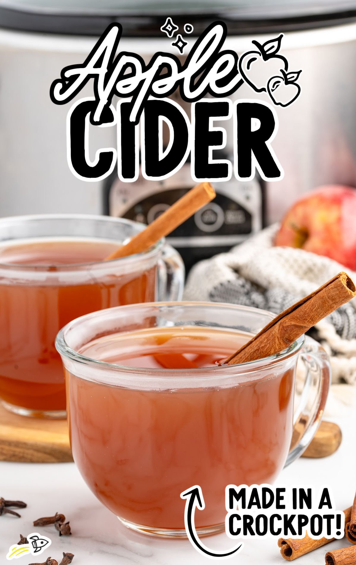 Homemade apple cider in clear mugs topped with apple slices, orange slices, star anise, and cinnamon sticks.