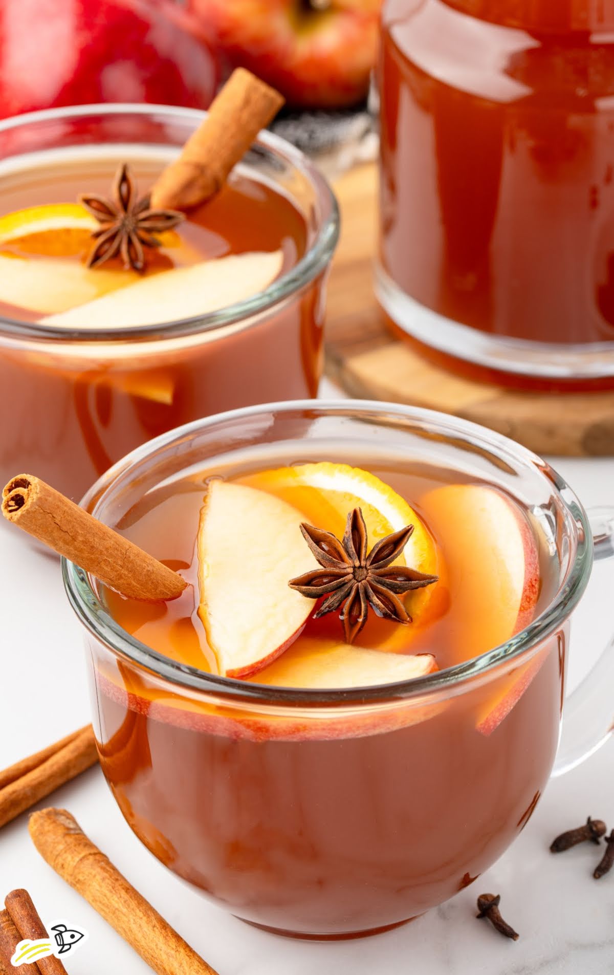 Cozy fall apple cider served in glass mugs with cinnamon sticks and star anise on a white countertop.