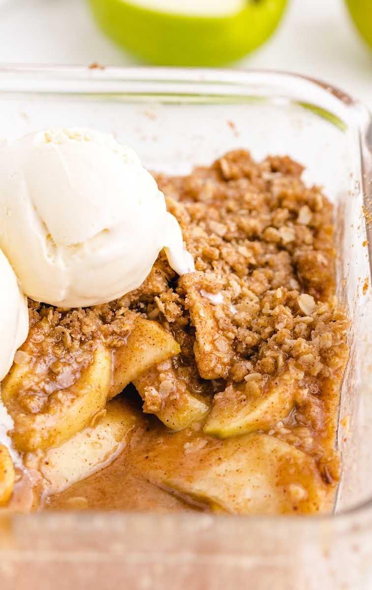 close up shot of apple crisp topped with scoops of vanilla ice cream in a baking dish
