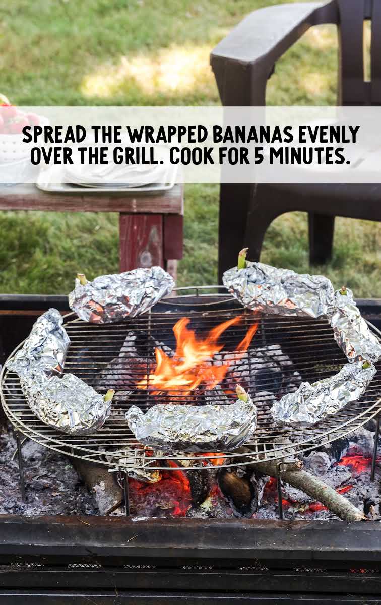 campfire banana boats process shot of aluminum foil wrapped bananas over a grill