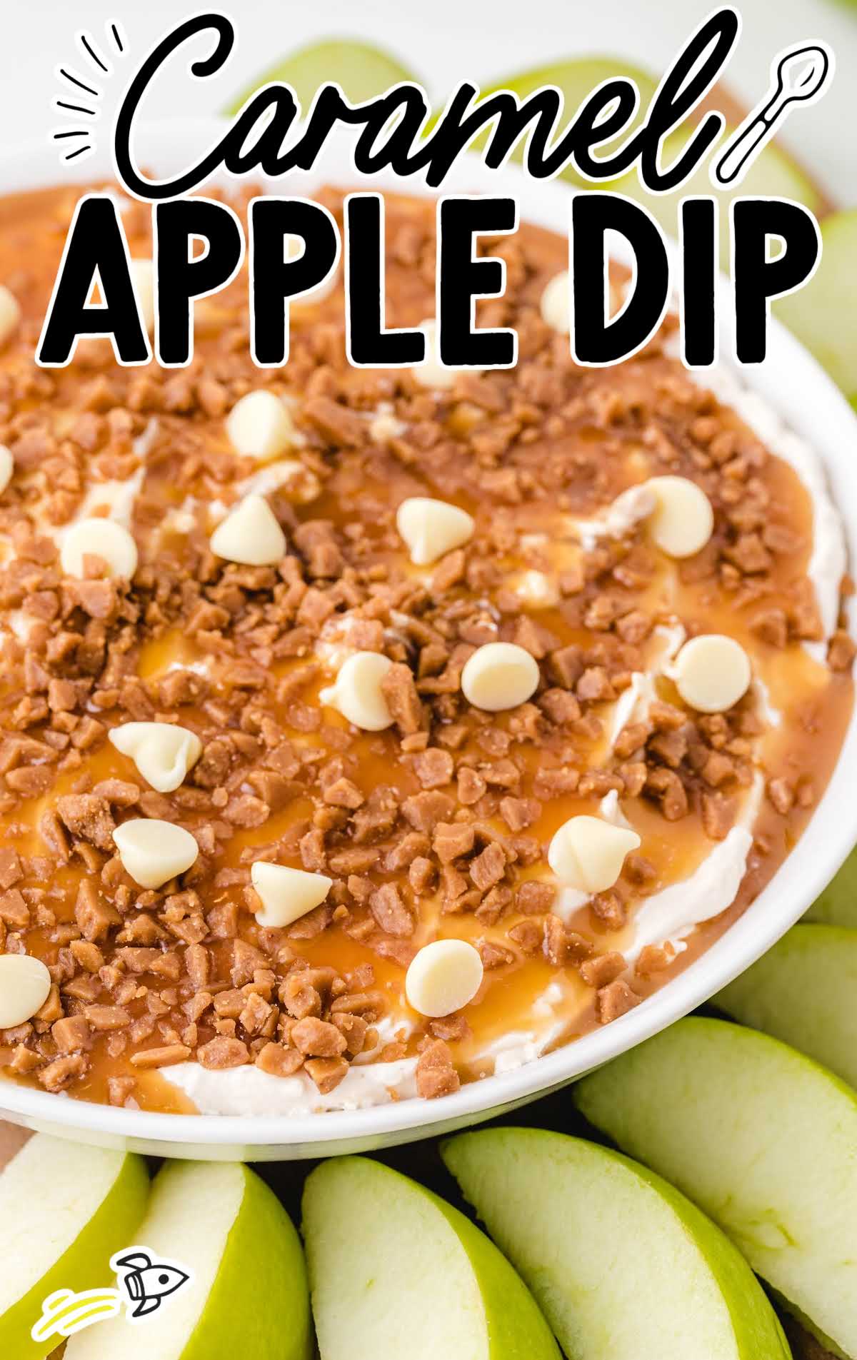close up shot of a bowl of caramel apple dip topped with caramel, toffee, and white chocolate with sliced apples on the side for dipping