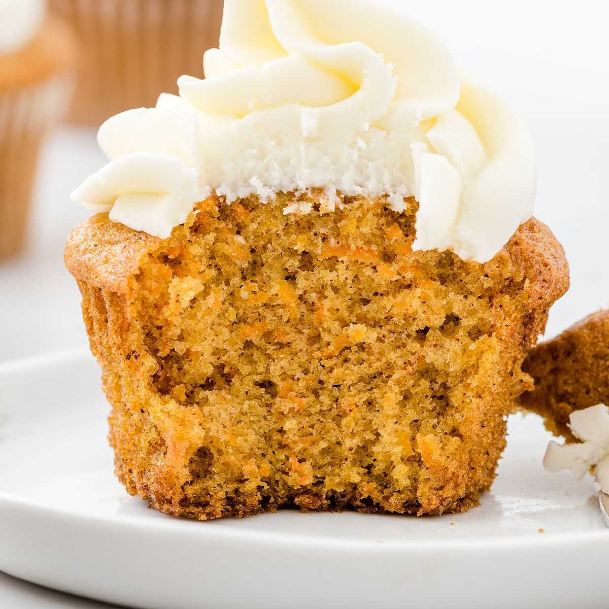 close up shot of a cupcake topped with frosting and a bite taken out of it on a plate