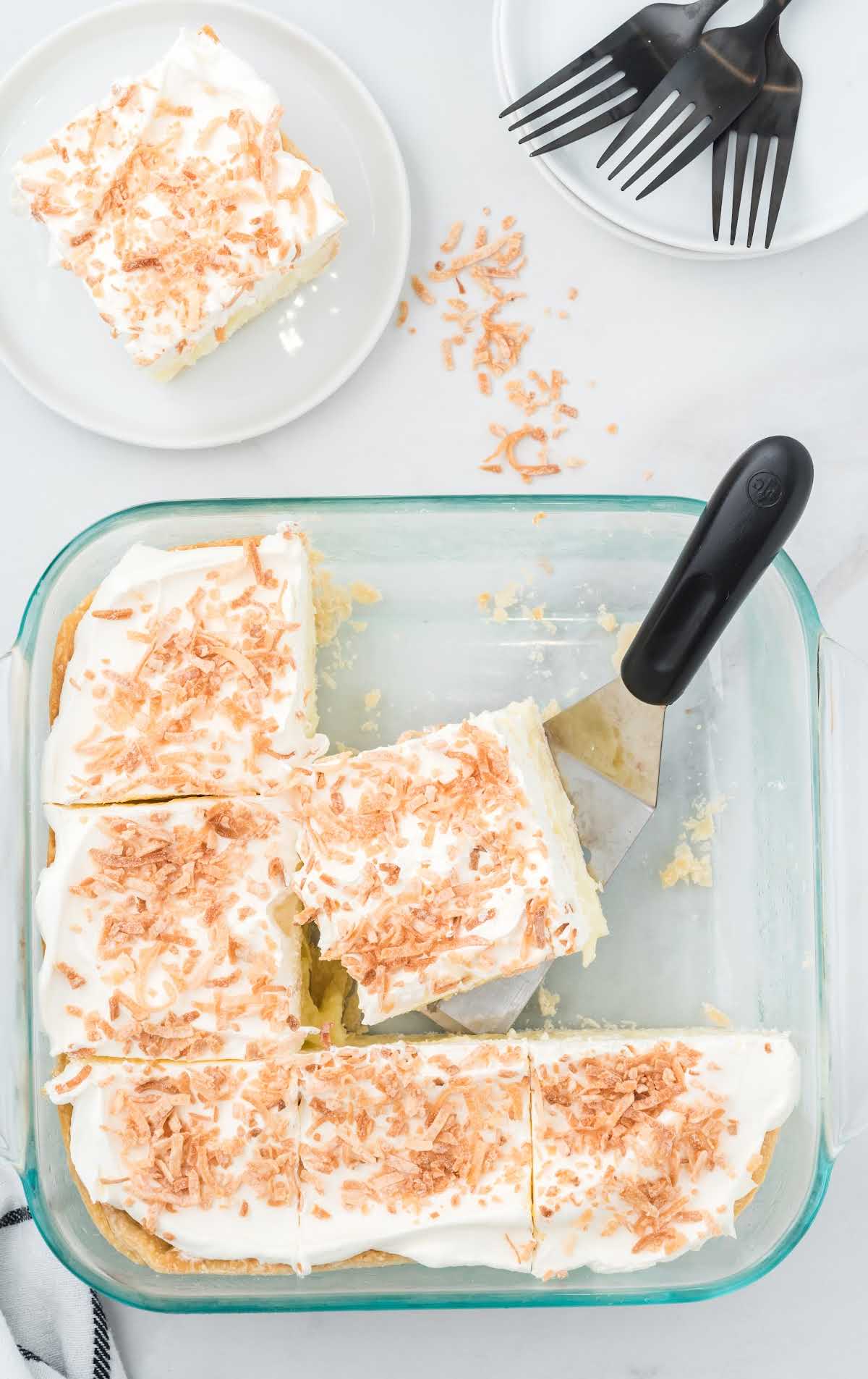 close up shot of coconut cream bars in a clear dish with a spatula