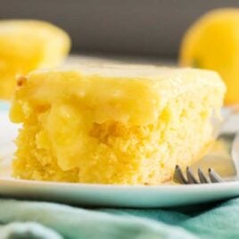 close up side shot of lemon poke cake on a white plate with a fork