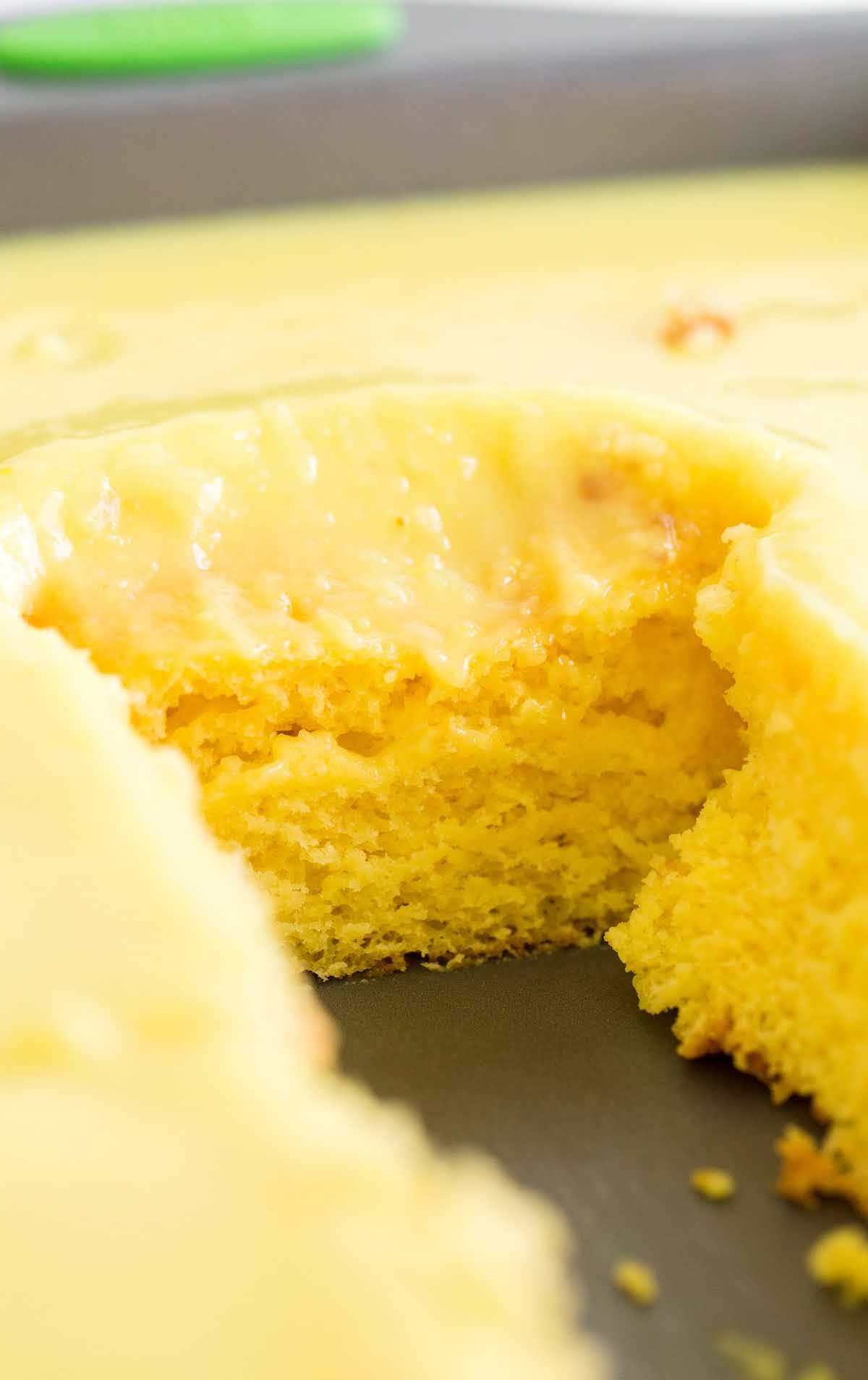 lemon poke cake in a pan with a slice taken off of it