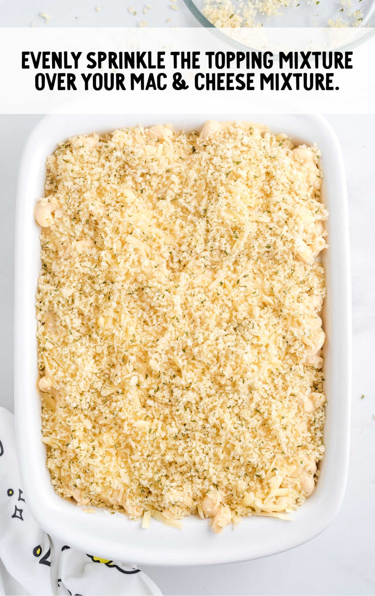 topping mixture being sprinkled over Mac and cheese in a casserole dish