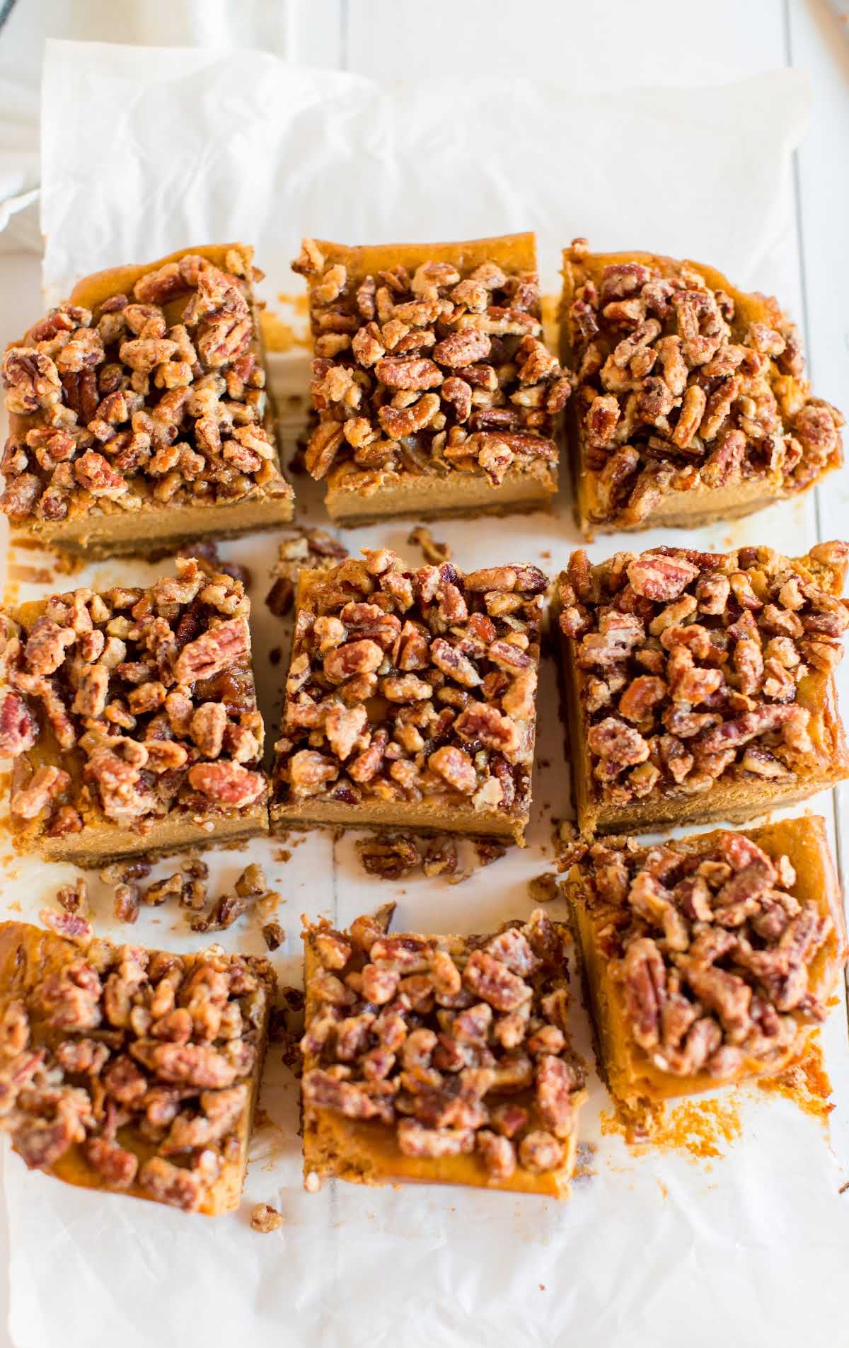 Pumpkin cheesecake bars cut into squares and topped with crunchy pecans on parchment paper