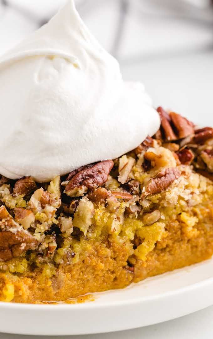 close up shot of a slice of Pumpkin Crunch Cake topped with whipped topping on a plate