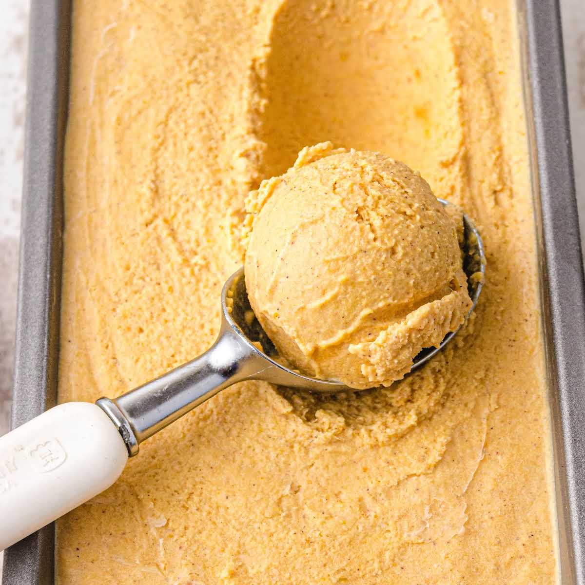 a scoop of pumpkin ice cream in a ice cream scooper and in a pan