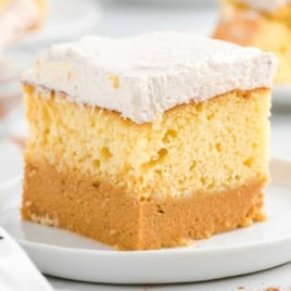 Pumpkin magic cake slice on white plate with whipped cream topping, showcasing distinct pumpkin and yellow cake layers.