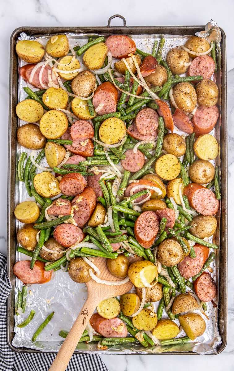 close up overhead shot of Sausage Green Bean Potato Casserole on a sheet pan with a wooden spoon