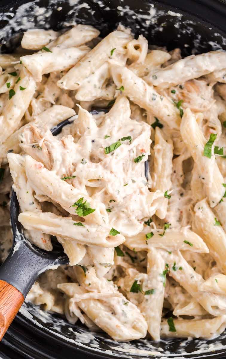 close up shot of Slow Cooker Olive Garden Chicken Pasta topped with parsley in a crockpot with a large spoon