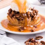 close up shot of hasselback apples topped with caramel, pecans, and vanilla ice cream on a plate