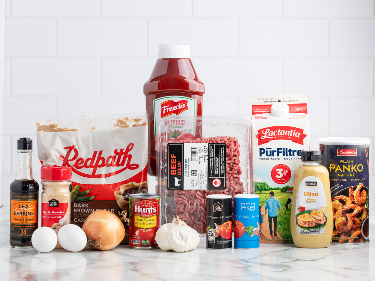 Ingredients for a Meatloaf recipe arranged on a counter, including ground beef, ketchup, brown sugar, milk, panko, Dijon mustard, Worcestershire sauce, eggs, onion, garlic, and tomato sauce.