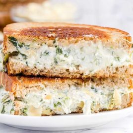 close up shot of slices of spinach artichoke grilled cheese stacked on top of each other on a plate