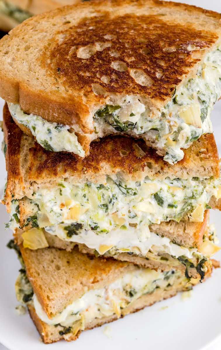 close up shot of slices of spinach artichoke grilled cheese stacked on top of each other