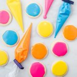 yellow, pink, blue, and orange icing in piping bags and also on top of sugar cookies