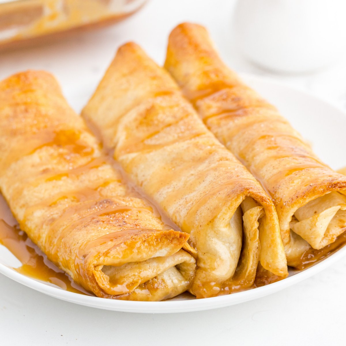 3 Apple enchiladas are on a small plate drizzled with caramel.