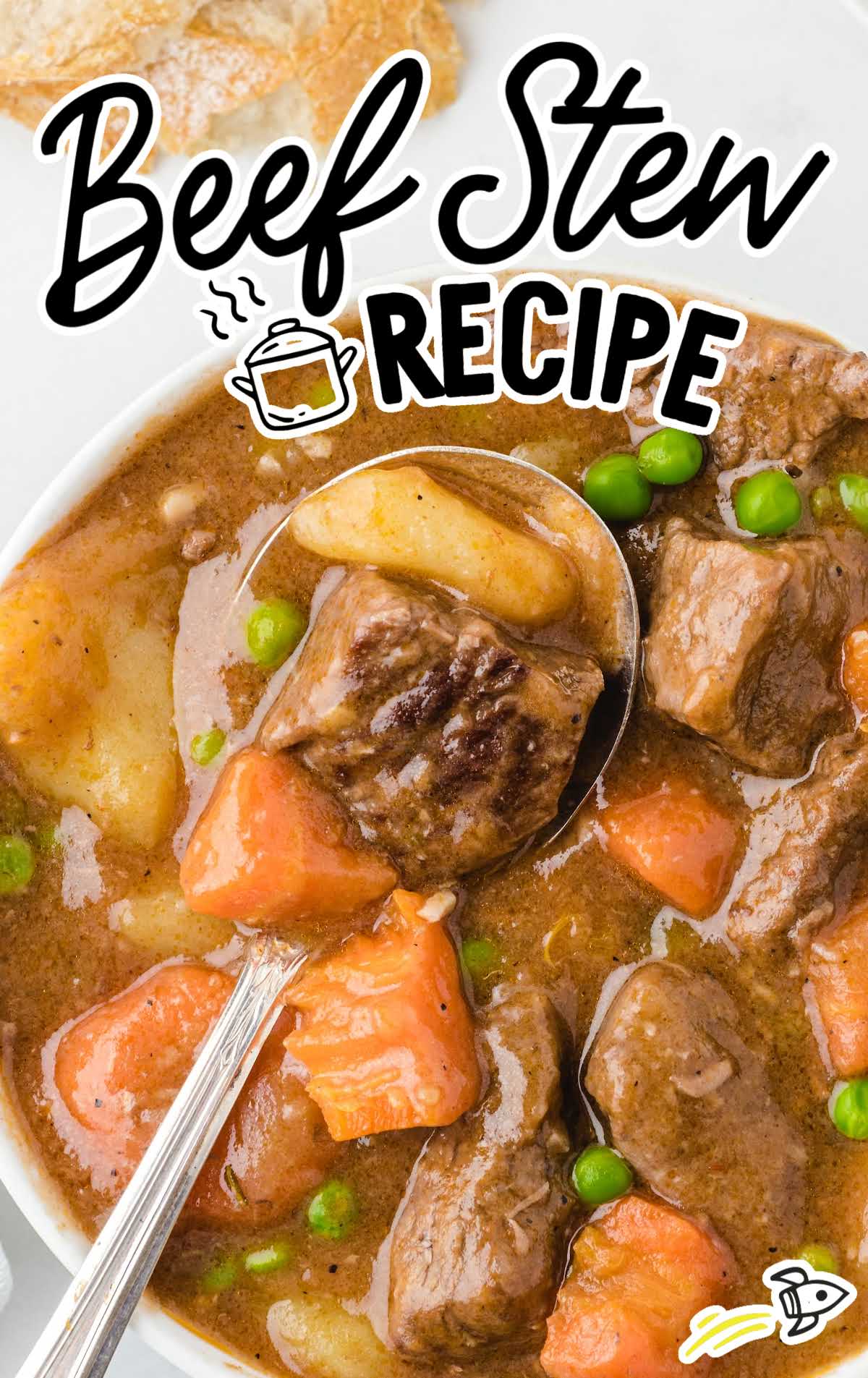Overhead view of beef stew in a bowl with a spoon, filled with chunks of beef, potatoes, carrots, and green peas.