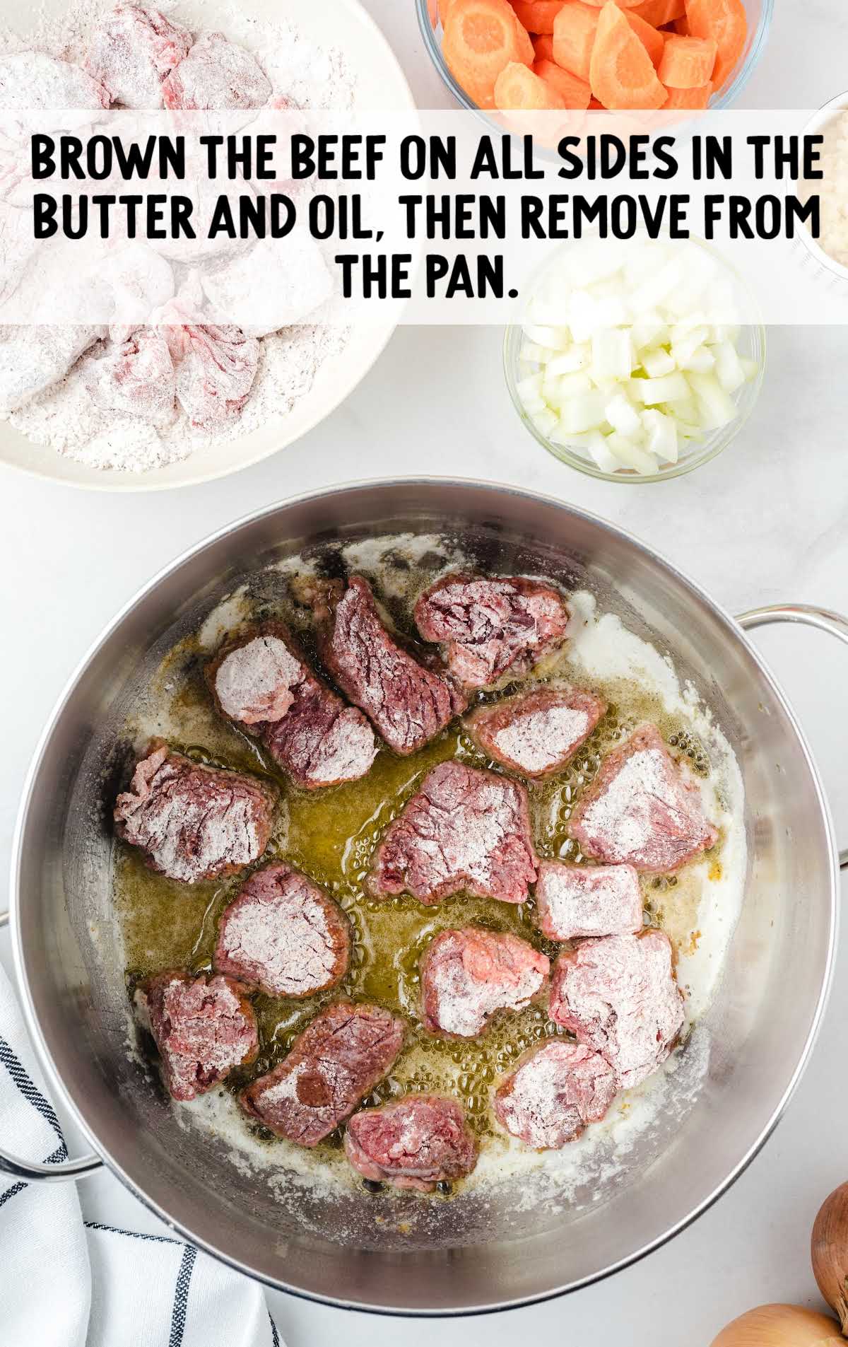Floured beef chunks browning in a pot with butter and oil, surrounded by fresh vegetables.