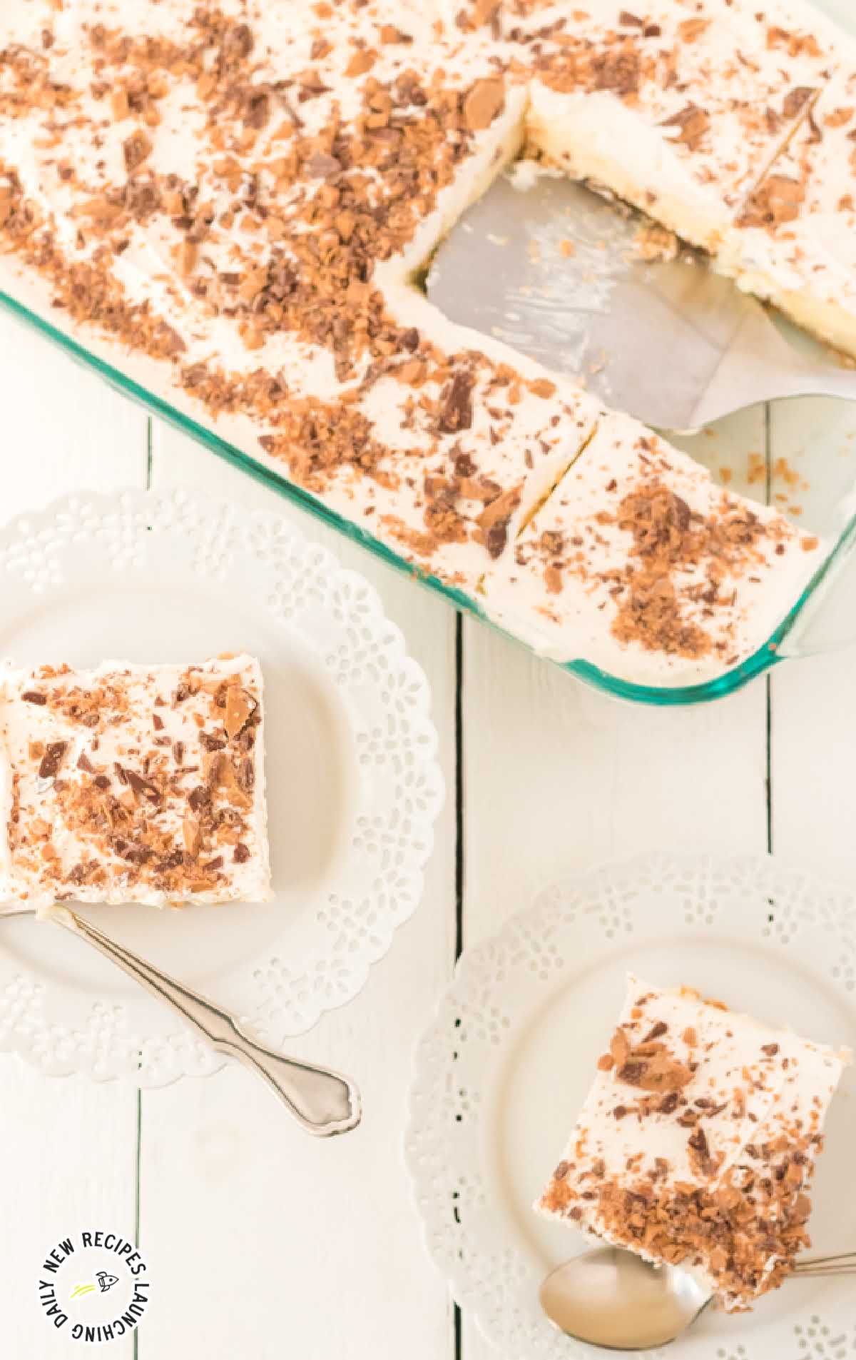 close up shot of a slices of butter pecan crunch topped with cool whip and crumbled heath candy bars on a plate and in a baking dish