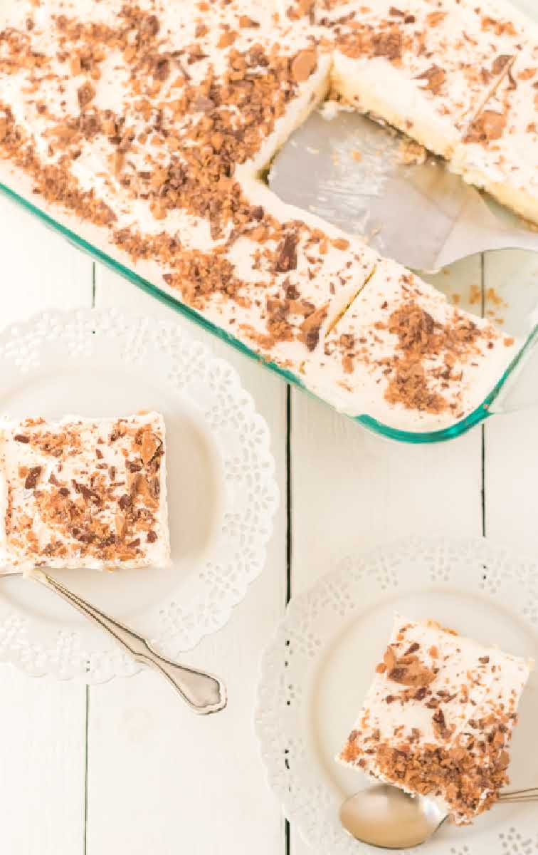 close up shot of a slices of butter pecan crunch topped with cool whip and crumbled heath candy bars on a plate and in a baking dish