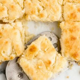 close up overhead shot of Butter Swim Biscuits in a baking dish with a biscuit being picked up with a spatula